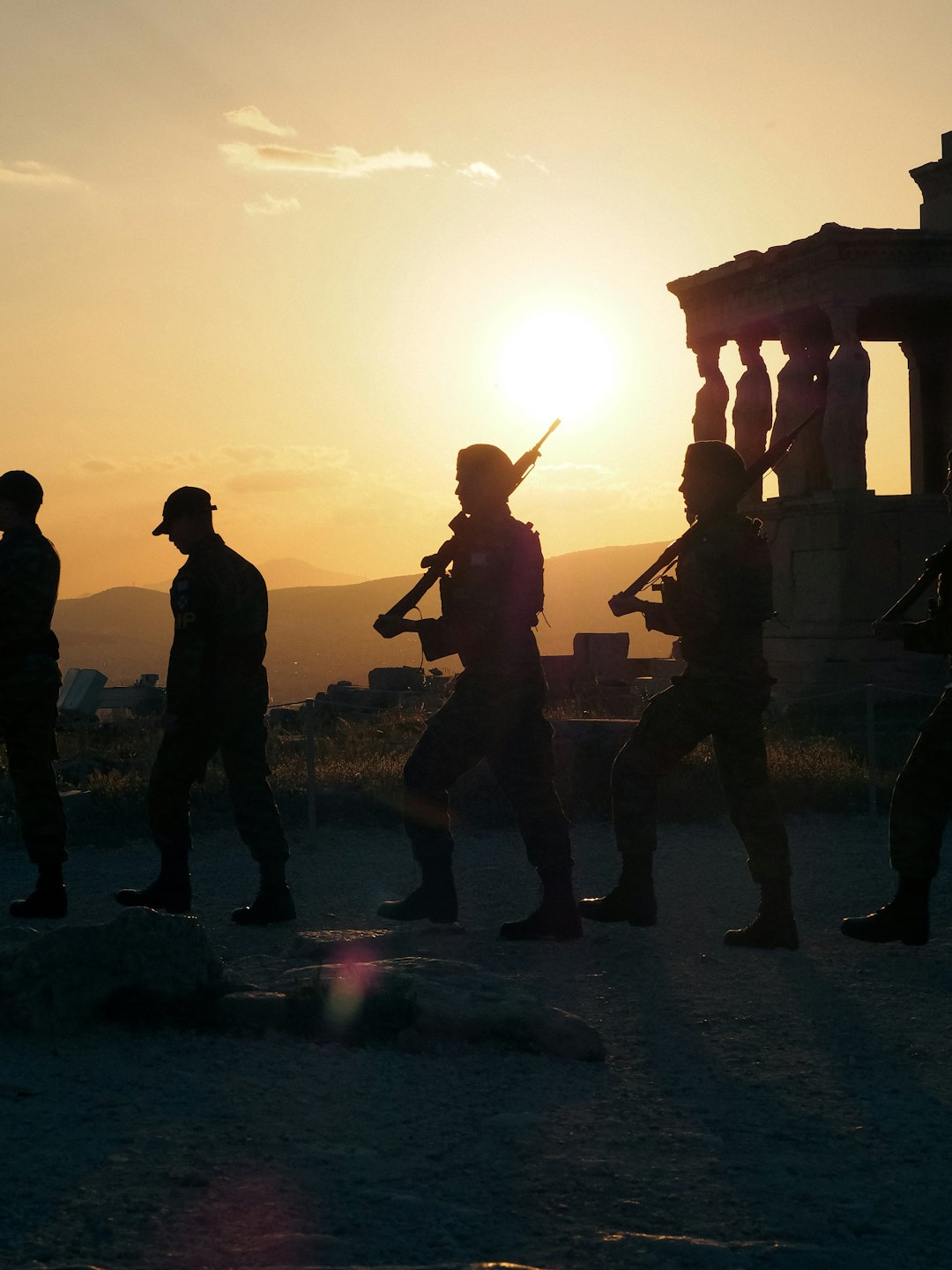 Soldaten in Silhouette marschieren bei Sonnenuntergang an antiken Ruinen vorbei.