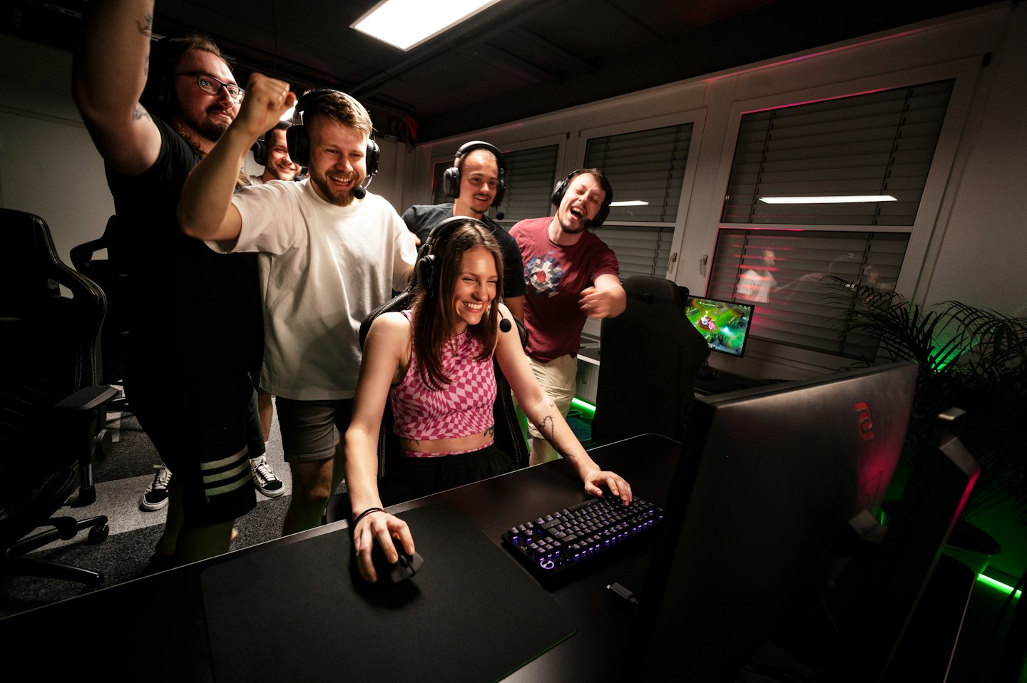 Eine Frau spielt Videospiele, während Männer um sie herum jubeln.