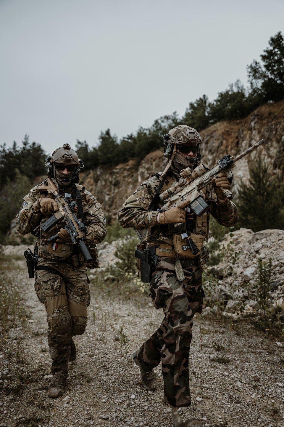 Zwei Soldaten in Tarnkleidung gehen über eine felsige Landschaft.